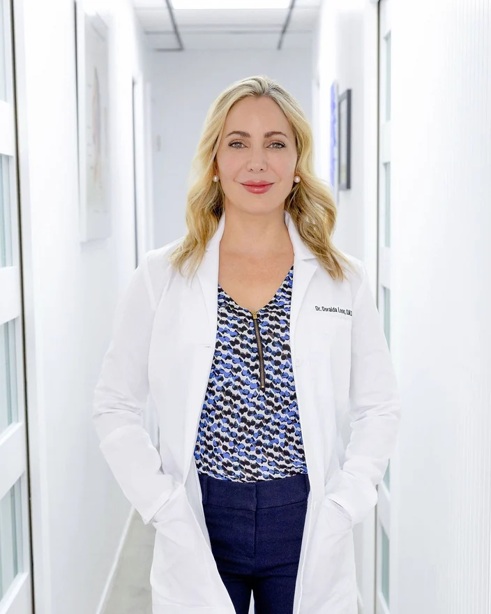Dr. Leon smiling in her white coat, in a close portrait in the office hallway